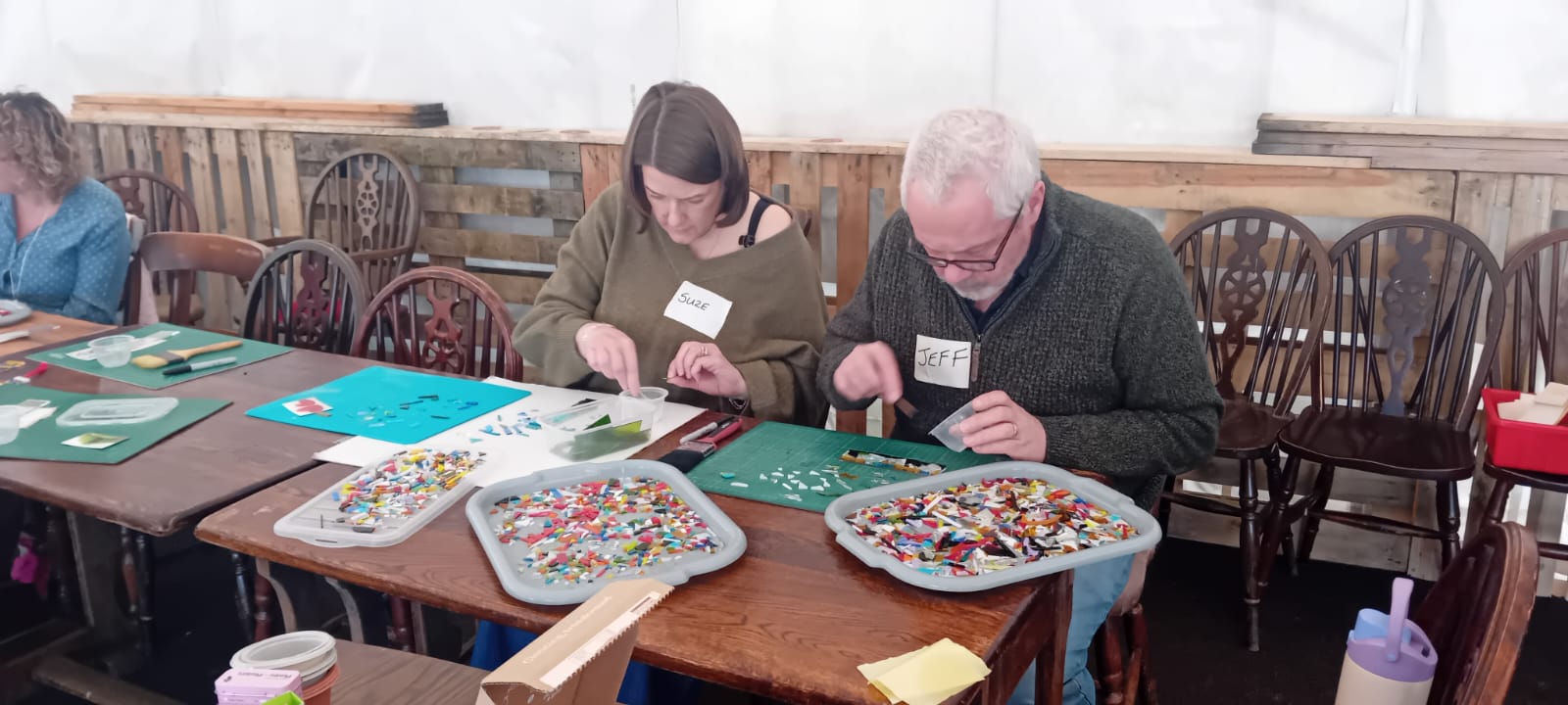 Two participants concentrating on glass mosaic pieces at a community workshop