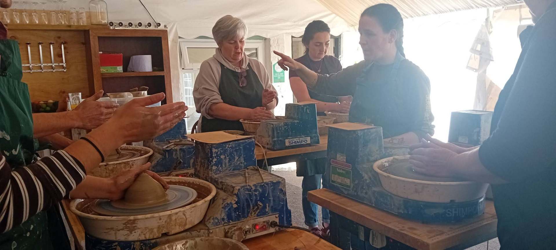 Participants throwing clay on pottery wheels under a tutor's guidance
