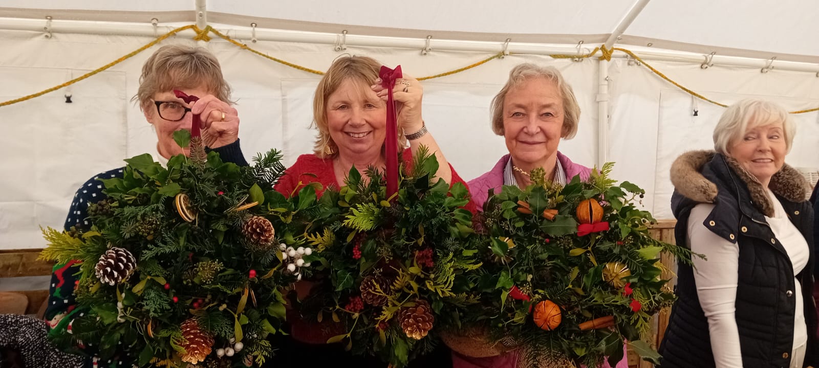 Three participants holding handmade Christmas wreaths at The Halfway
